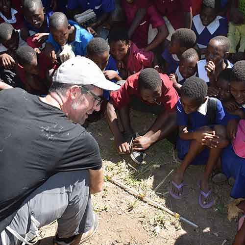 Dr Graham Walker with kids in Africa, squatting on the ground with an experiment