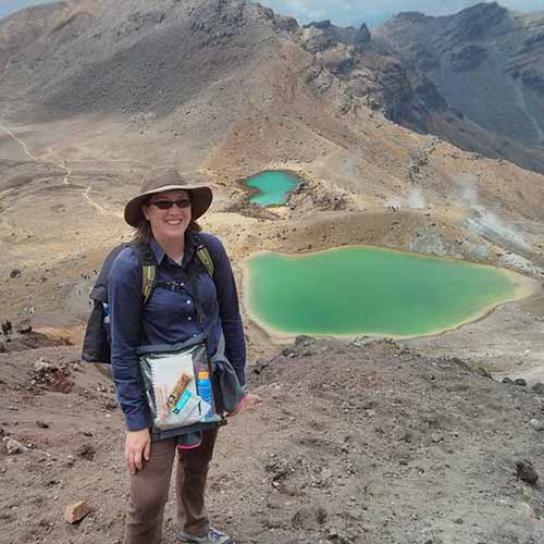 Alyssa Weirman standing at the Tongariro crossing. There is a lake in the distance below her 