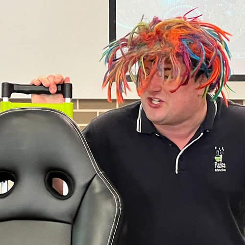 A man wearing a colourful wig behind a car seat